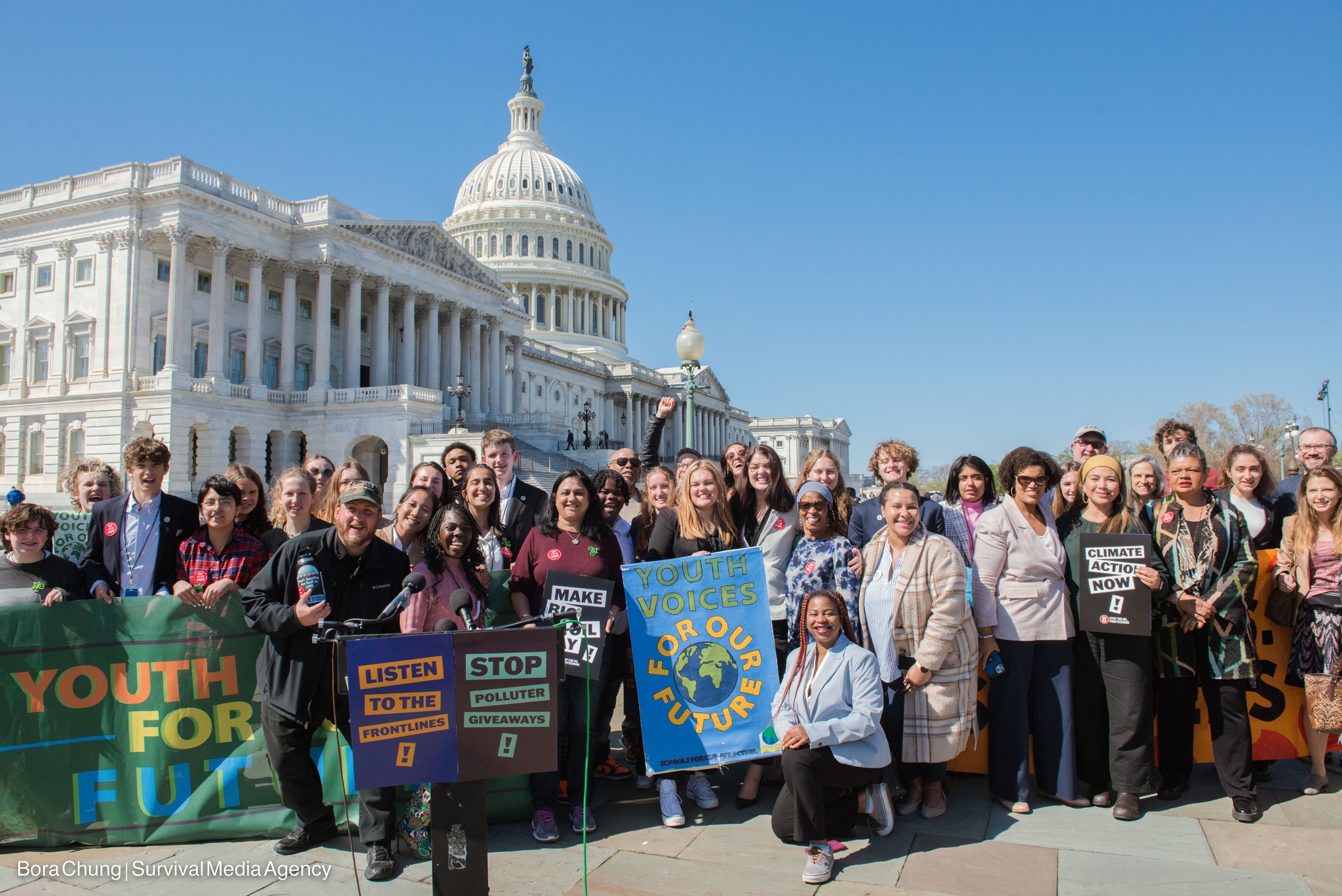 Group of diverse people standing in front of the U.S. Capitol holding signs denouncing fossil fuels and demanding Climate Action.